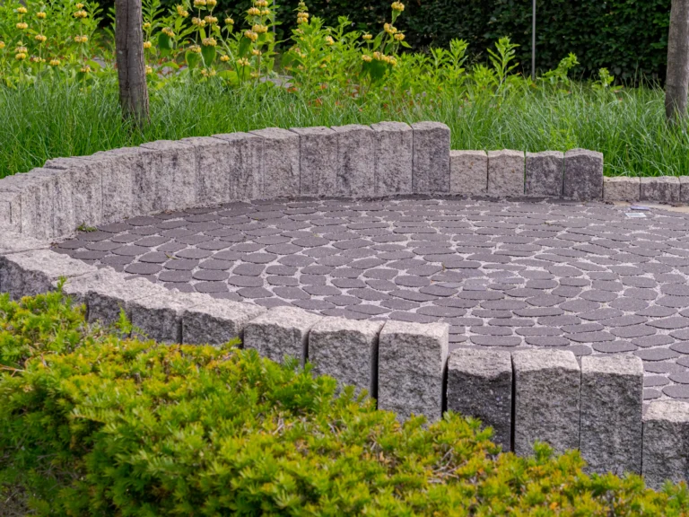 Circular paver patio with a curved stone seat wall and green shrubs