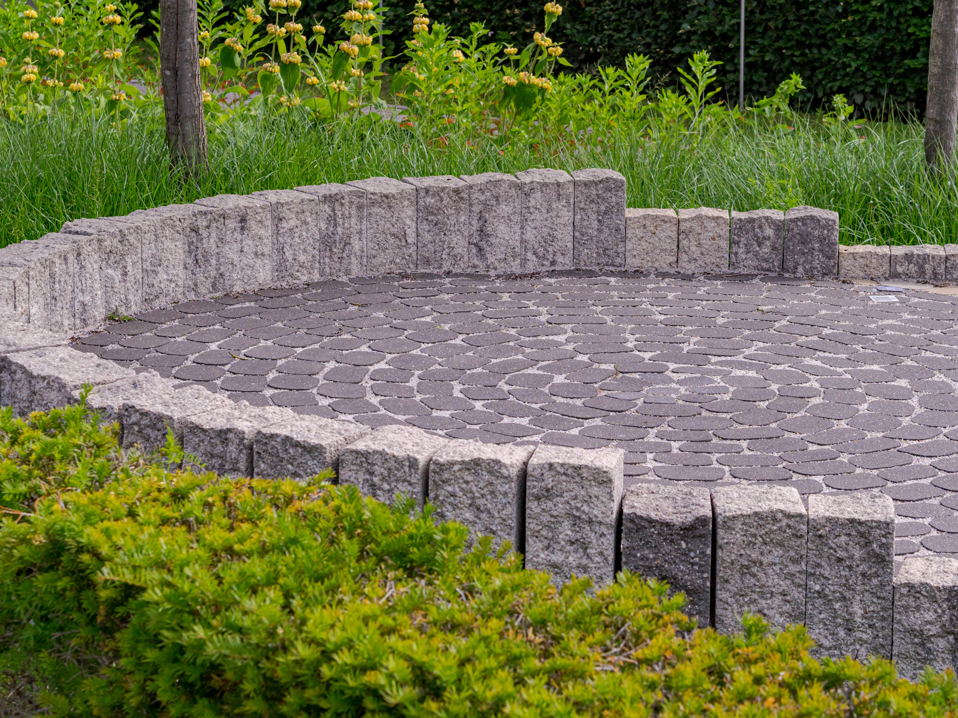 Circular paver patio with a curved stone seat wall and green shrubs